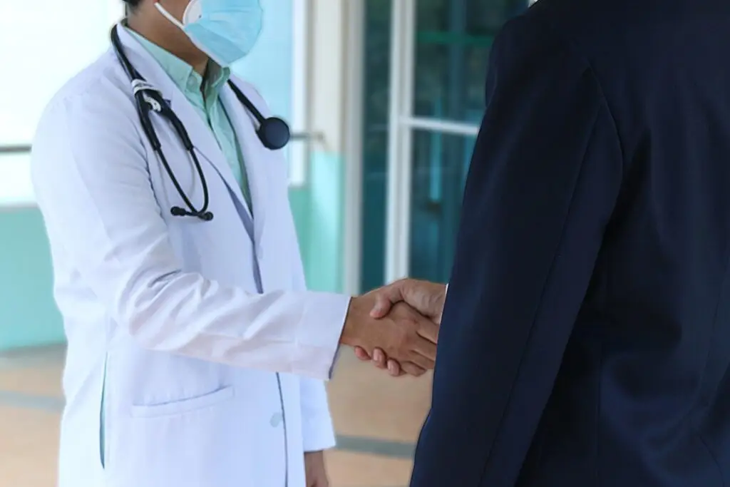 Male Doctor wearing surgical mask and shaking hands with A Medical Billing Service Executive after a successful negotiation on billing rates and services.